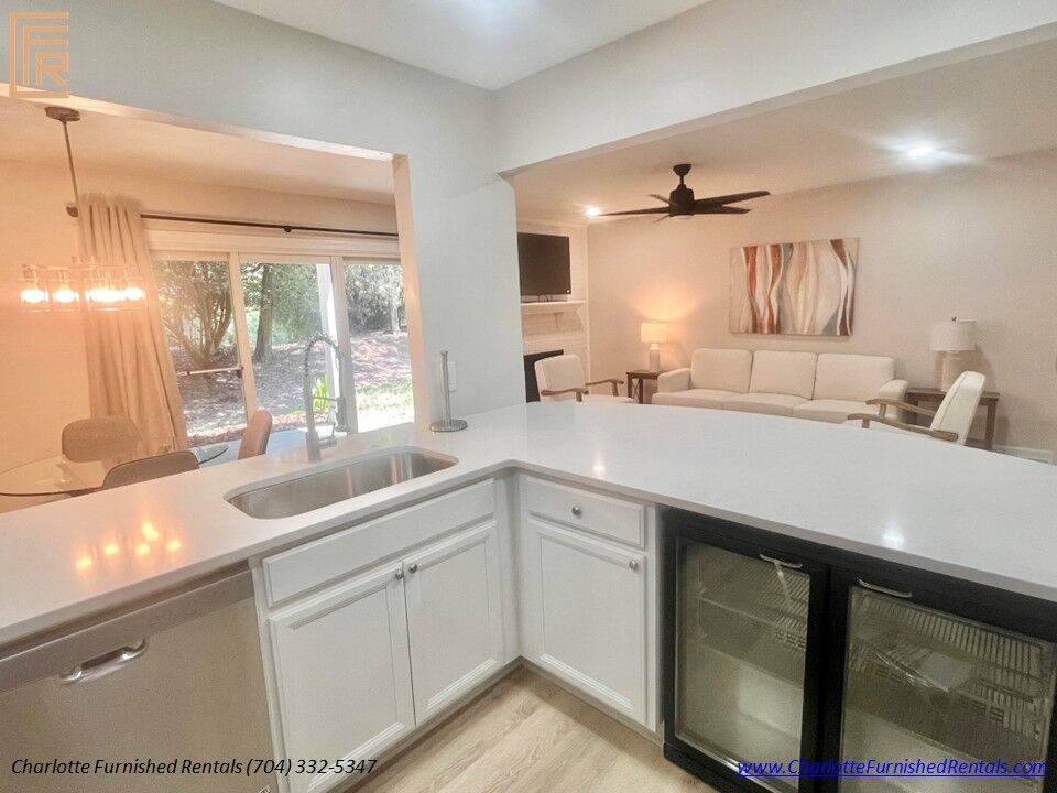 Modern Open Kitchen & Living Room – 9427 South Vicksburg Park Court Open-concept kitchen with quartz countertops, breakfast bar, beverage refrigerator and furnished living room at Charlotte Furnished Rentals' SouthPark home.