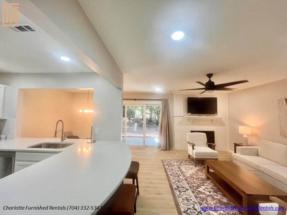 Open Living Area with Fireplace Open living room featuring fireplace, mounted television, breakfast bar and patio access in furnished SouthPark Charlotte home.