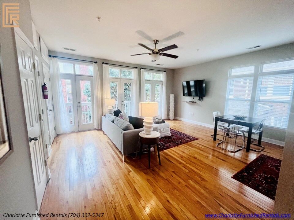 Slide6 Living Room Bright, professionally furnished living room with comfortable seating and natural light. Open-concept living area featuring modern furnishings and hardwood-style flooring. Comfortable living room with mounted television and adjoining dining area.